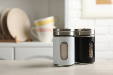 Photo of Salt and pepper shakers on light wooden table in kitchen, closeup. Space for text