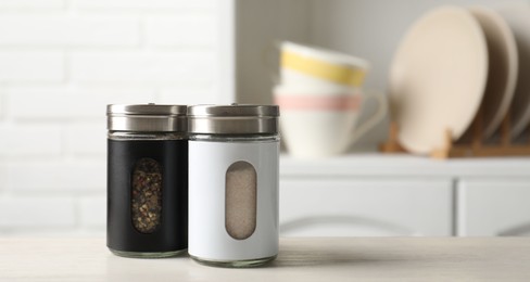 Photo of Salt and pepper shakers on light wooden table in kitchen, closeup. Space for text