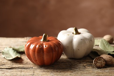 Photo of Salt, pepper shakers in shape of pumpkins, dry bay leaves and nutmegs on wooden table against blurred brown background, closeup