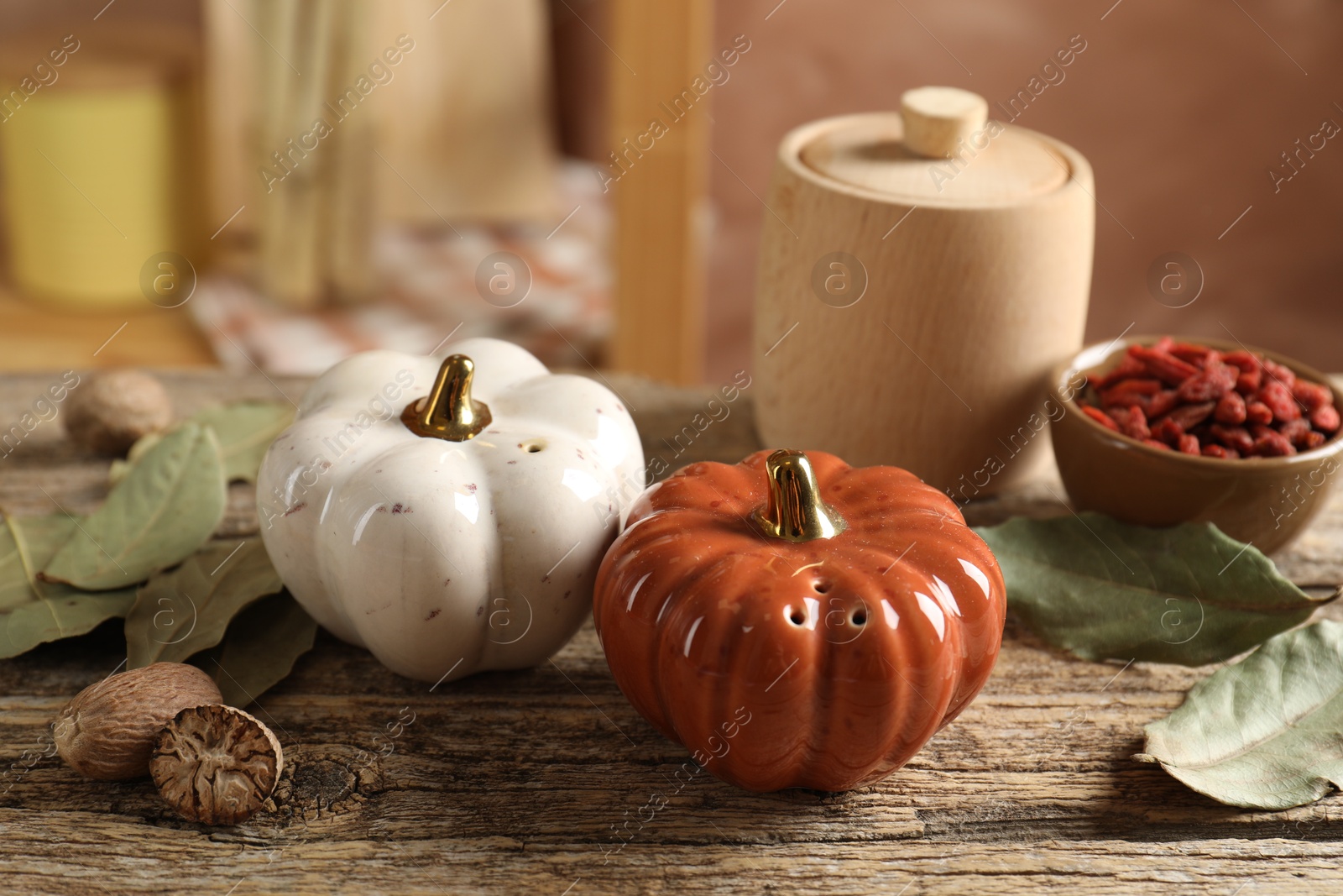 Photo of Salt, pepper shakers in shape of pumpkins and spices on wooden table against blurred brown background, closeup