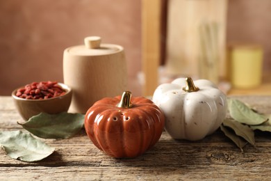 Photo of Salt, pepper shakers in shape of pumpkins and spices on wooden table against blurred brown background, closeup