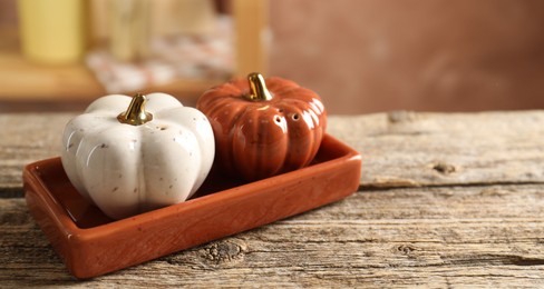 Photo of Salt and pepper shakers in shape of pumpkins on wooden table against blurred brown background, closeup. Space for text