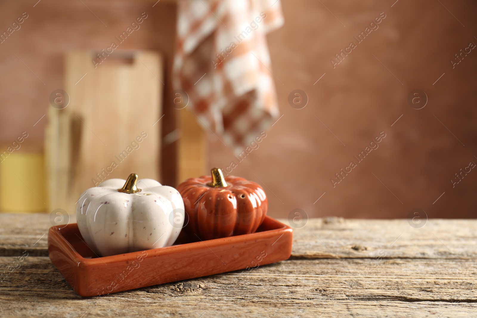 Photo of Salt and pepper shakers in shape of pumpkins on wooden table in kitchen, closeup. Space for text
