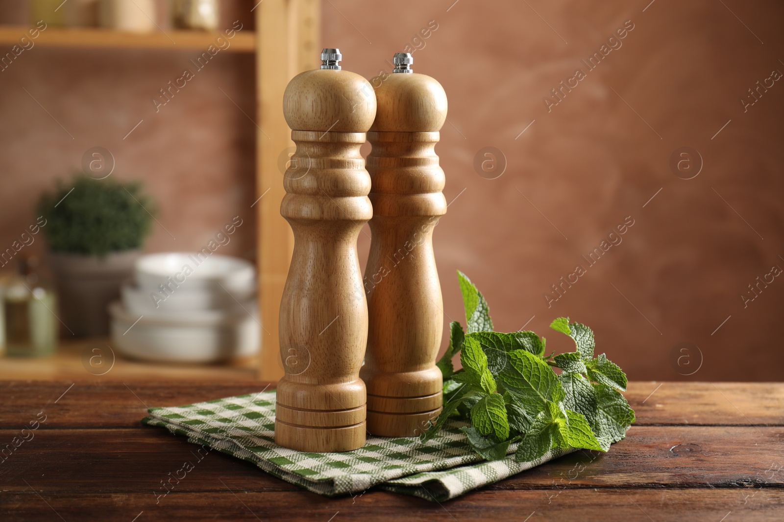 Photo of Salt, pepper mills, mint and napkin on wooden table in kitchen, closeup