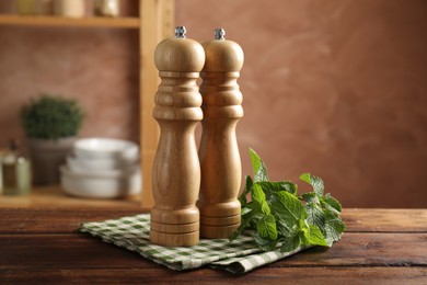 Photo of Salt, pepper mills, mint and napkin on wooden table in kitchen, closeup