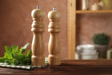 Photo of Salt, pepper mills, mint and napkin on wooden table in kitchen, closeup. Space for text