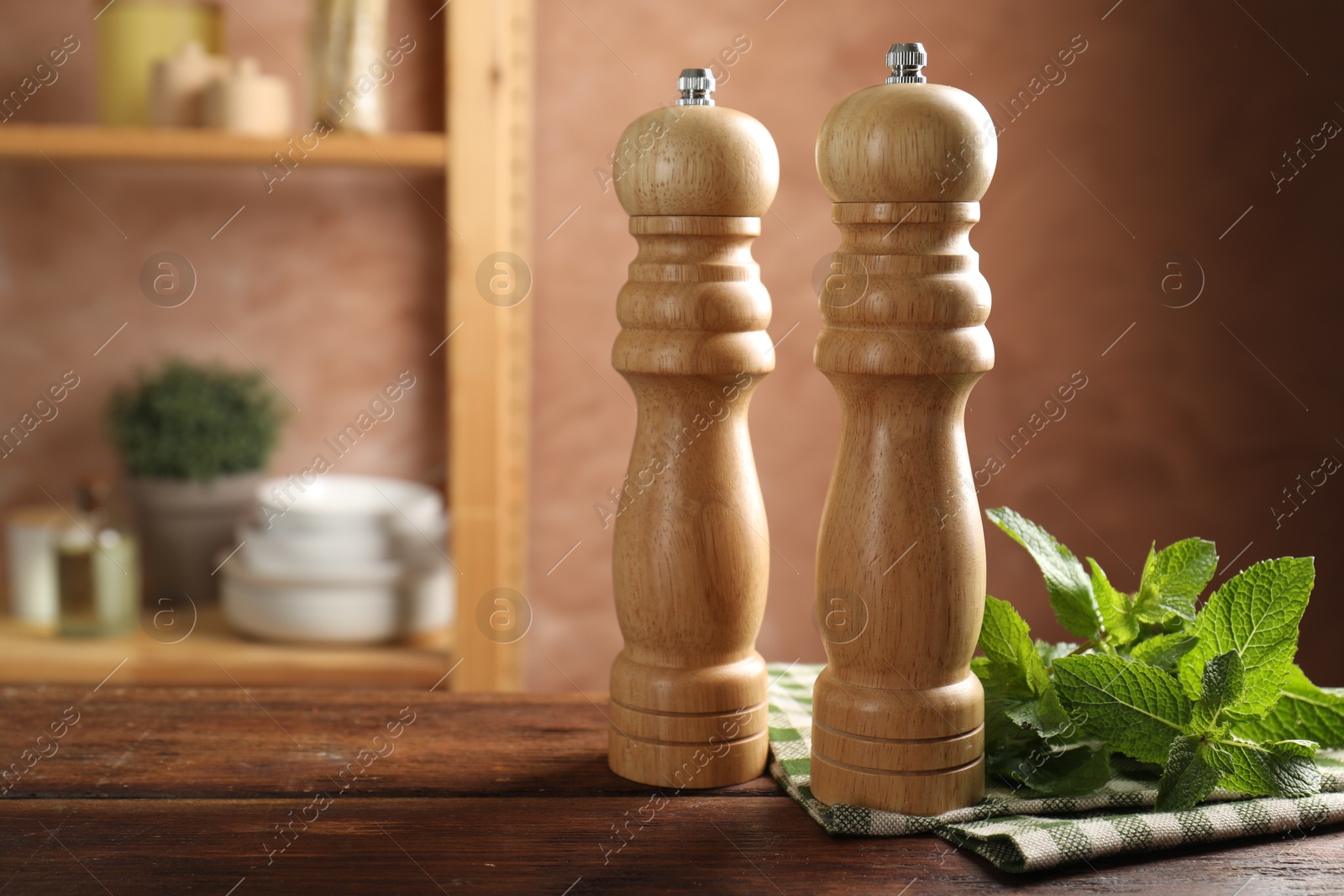 Photo of Salt, pepper mills, mint and napkin on wooden table in kitchen, closeup. Space for text