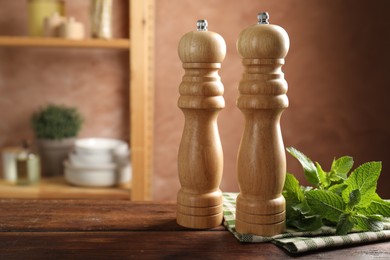 Photo of Salt, pepper mills, mint and napkin on wooden table in kitchen, closeup. Space for text
