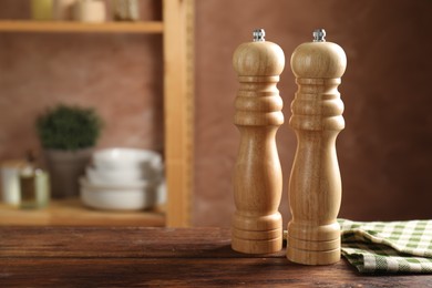 Photo of Salt and pepper mills on wooden table in kitchen, closeup. Space for text