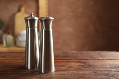 Photo of Metal salt and pepper shakers on wooden table in kitchen, closeup. Space for text