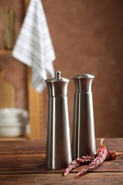 Photo of Metal salt, pepper shakers and dry chili peppers on wooden table in kitchen