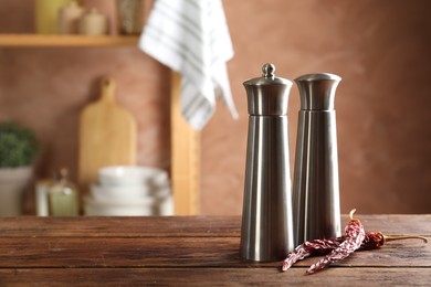 Photo of Metal salt, pepper shakers and dry chili peppers on wooden table in kitchen, closeup. Space for text
