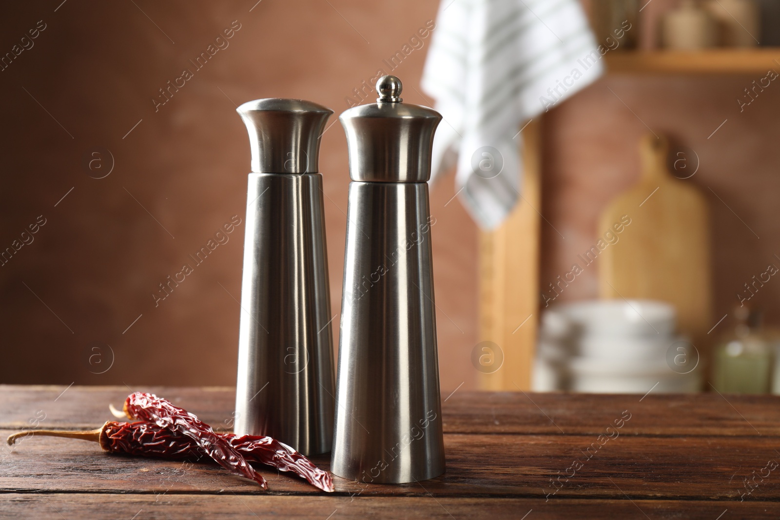 Photo of Metal salt, pepper shakers and dry chili peppers on wooden table in kitchen, closeup