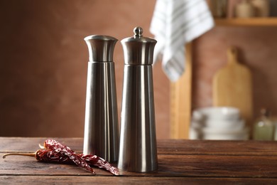 Photo of Metal salt, pepper shakers and dry chili peppers on wooden table in kitchen, closeup