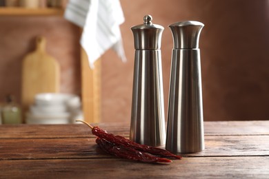 Photo of Metal salt, pepper shakers and dry chili peppers on wooden table in kitchen, closeup. Space for text