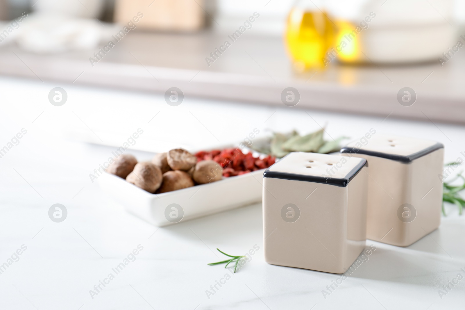 Photo of Salt, pepper shakers and spices on white marble table indoors, closeup. Space for text
