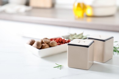 Photo of Salt, pepper shakers and spices on white marble table indoors, closeup. Space for text
