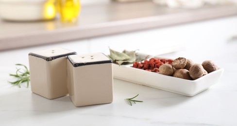 Photo of Salt, pepper shakers and spices on white marble table indoors, closeup