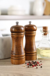 Photo of Salt, pepper mills, peppercorns and oil on wooden table indoors, closeup