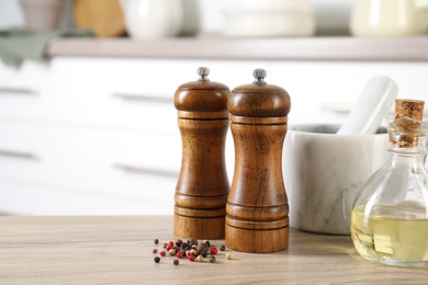 Photo of Salt, pepper mills, peppercorns, mortar and oil on wooden table indoors, closeup. Space for text