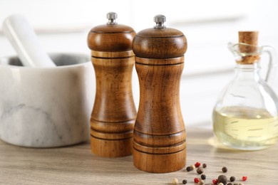Photo of Salt, pepper mills, peppercorns, mortar and oil on wooden table indoors, closeup