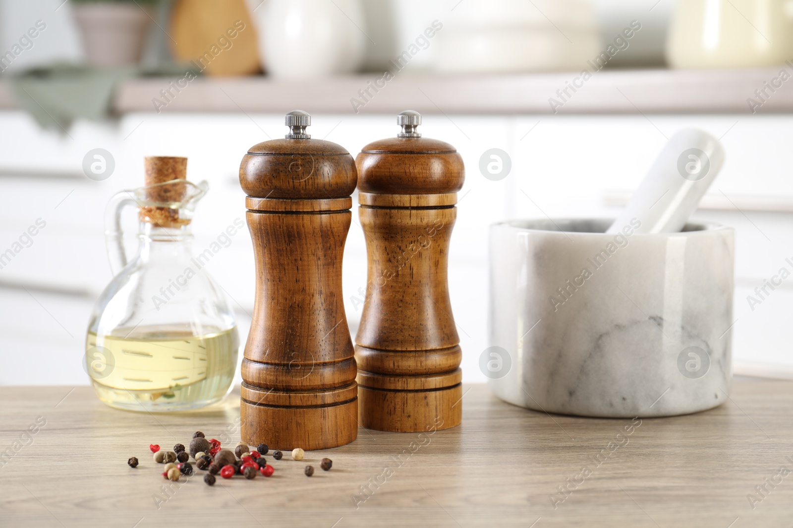 Photo of Salt, pepper mills, peppercorns, mortar and oil on wooden table indoors, closeup