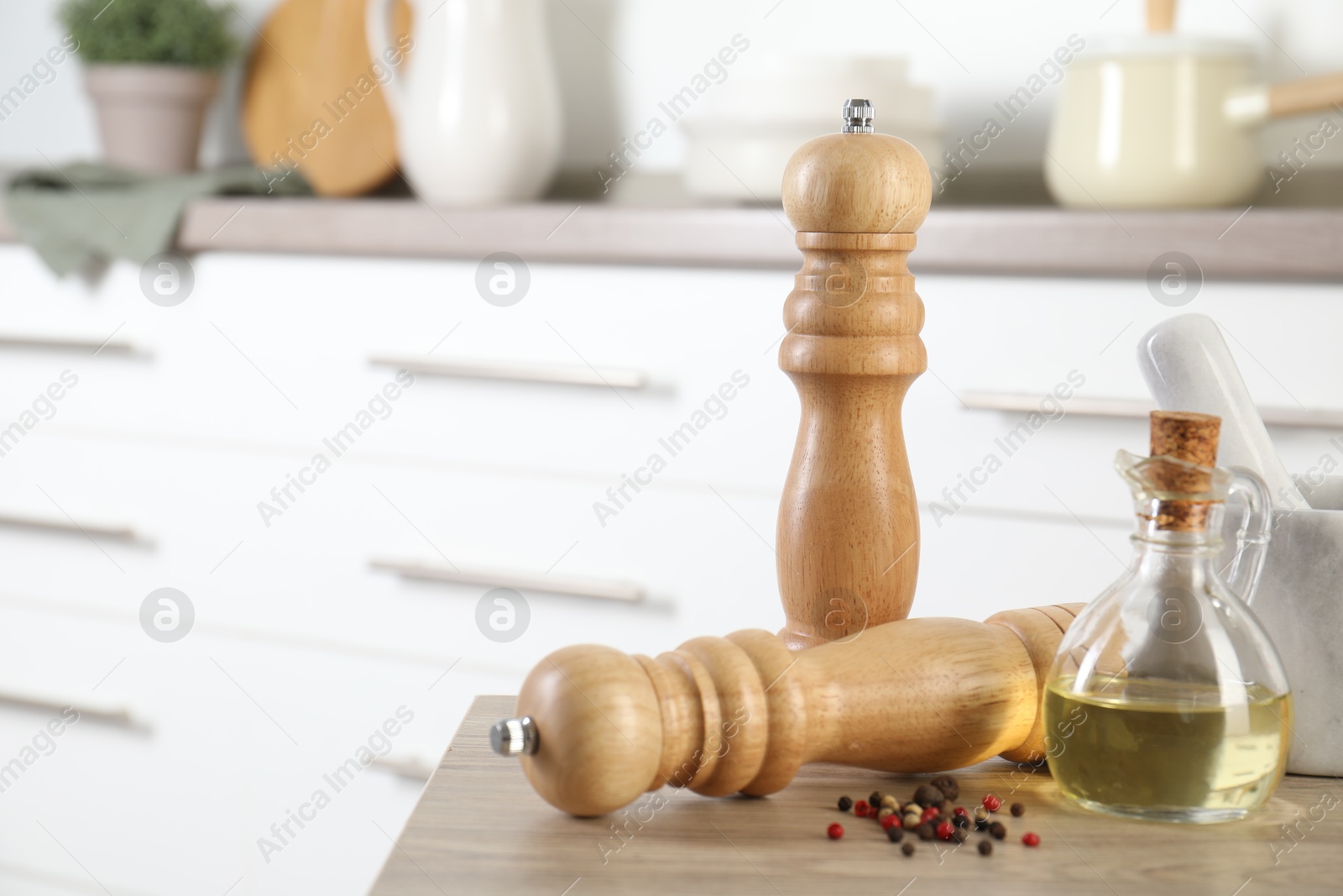 Photo of Salt, pepper mills, peppercorns, mortar and oil on wooden table in kitchen, closeup. Space for text