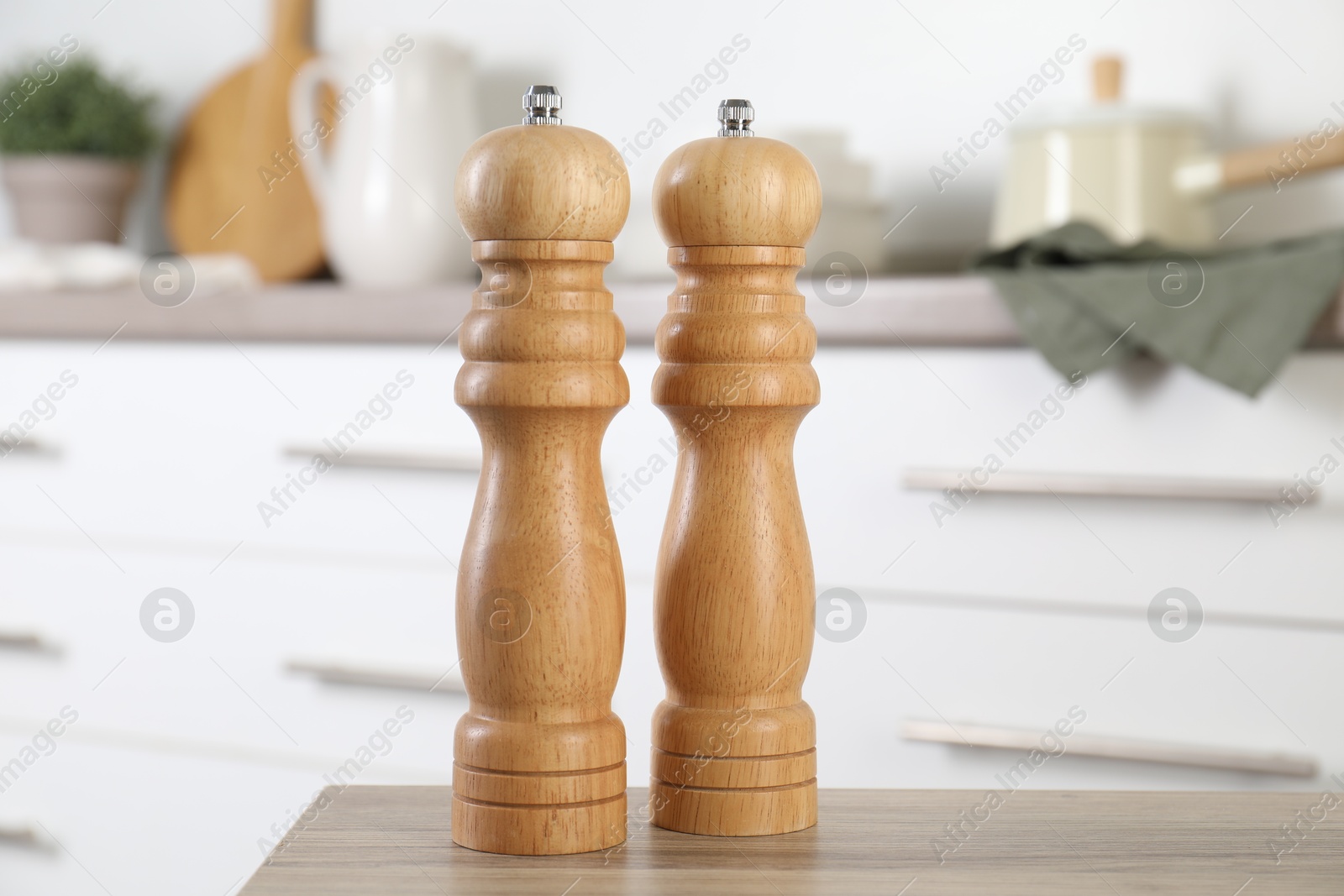 Photo of Salt and pepper mills on wooden table in kitchen, closeup
