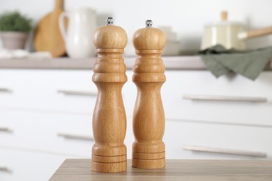 Photo of Salt and pepper mills on wooden table in kitchen, closeup