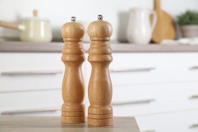 Photo of Salt and pepper mills on wooden table in kitchen, closeup. Space for text