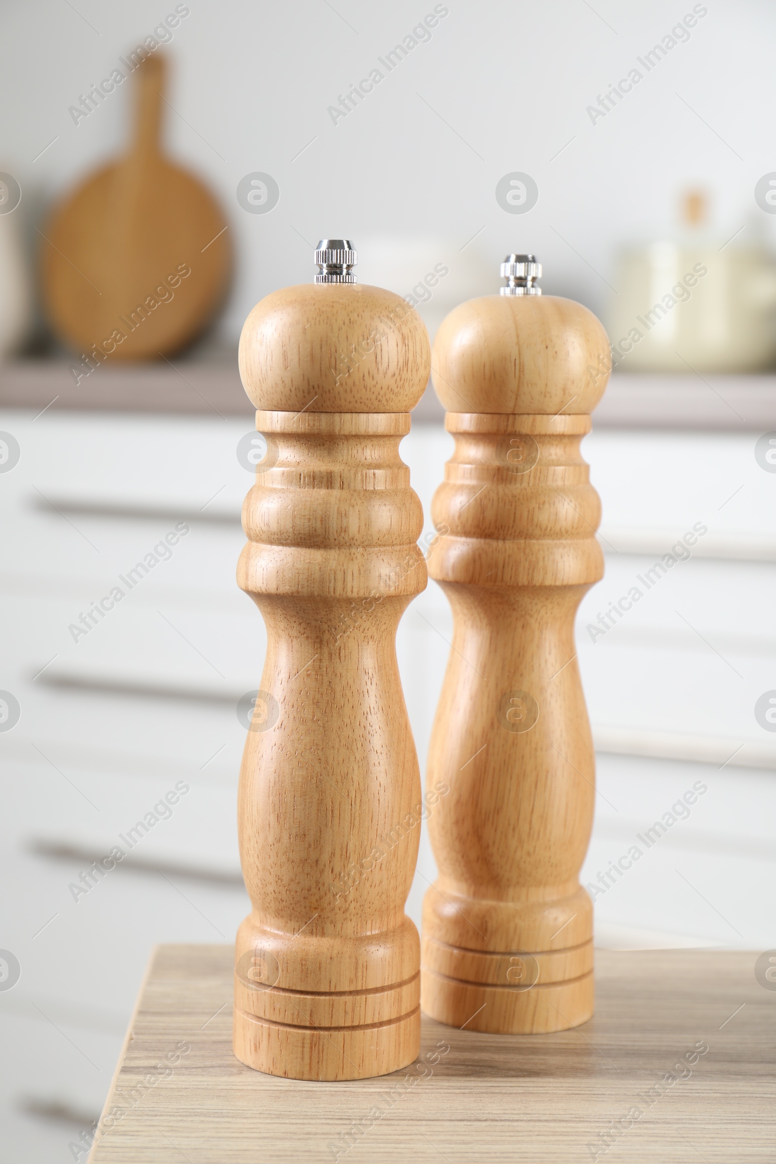 Photo of Salt and pepper mills on wooden table in kitchen, closeup