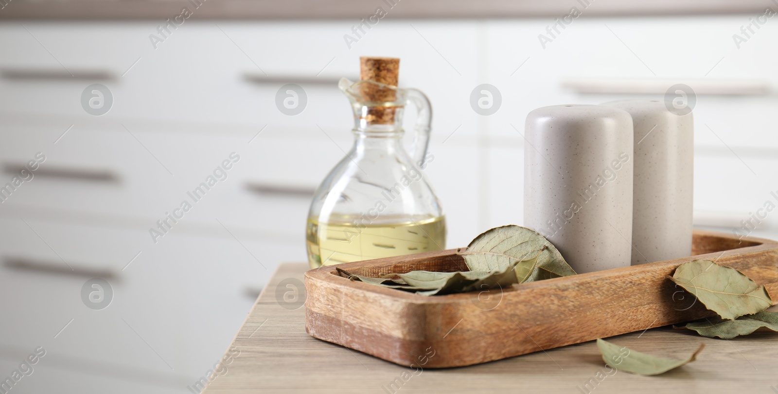 Photo of Salt and pepper shakers, dry bay leaves and bottle of oil on wooden table indoors, closeup. Space for text