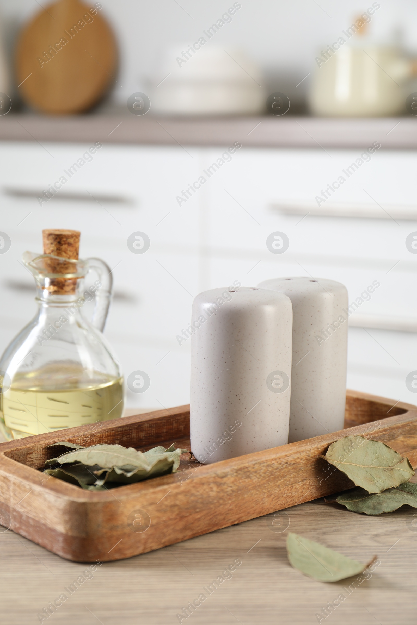 Salt and pepper shakers, dry bay leaves and bottle of oil on wooden table in kitchen, closeup Photo of Salt and pepper shakers, dry bay leaves and bottle of oil on wooden table in kitchen, closeup