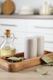 Photo of Salt and pepper shakers, dry bay leaves and bottle of oil on wooden table in kitchen, closeup
