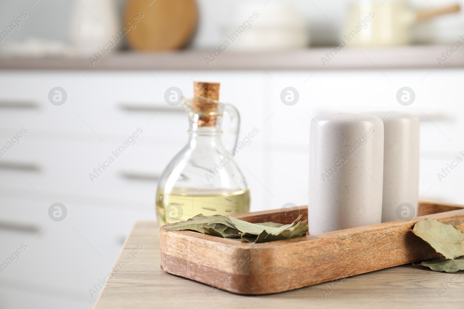 Photo of Salt and pepper shakers, dry bay leaves and bottle of oil on wooden table indoors, closeup. Space for text