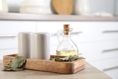 Photo of Salt and pepper shakers, dry bay leaves and bottle of oil on wooden table indoors, closeup
