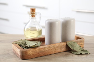 Photo of Salt and pepper shakers, dry bay leaves and bottle of oil on wooden table indoors, closeup