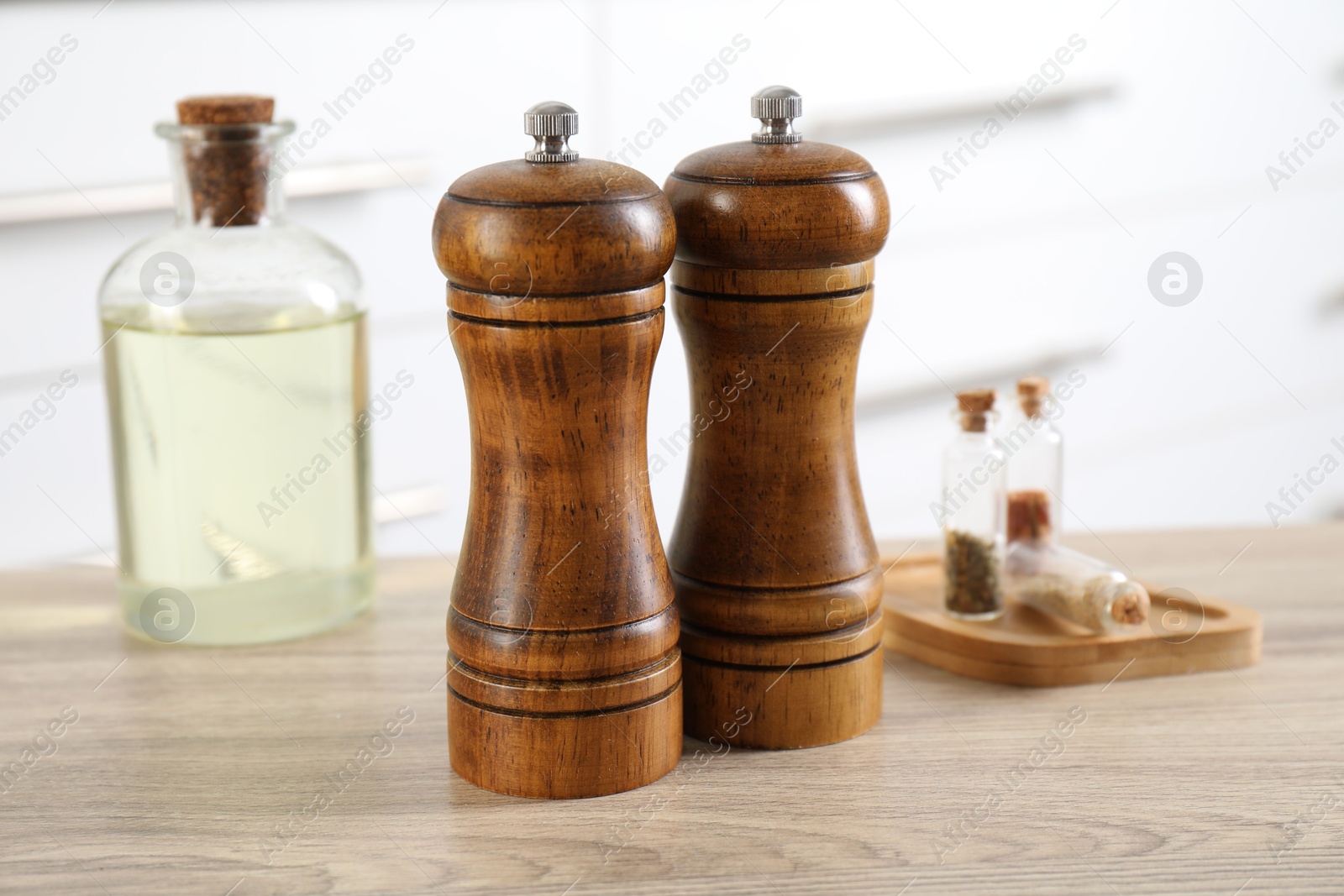Photo of Salt and pepper mills, spices and bottle of oil on wooden table indoors, closeup
