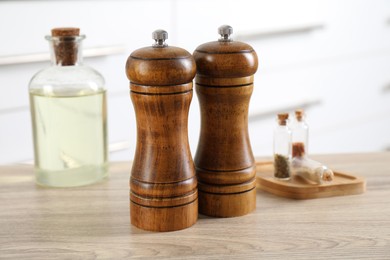 Photo of Salt and pepper mills, spices and bottle of oil on wooden table indoors, closeup
