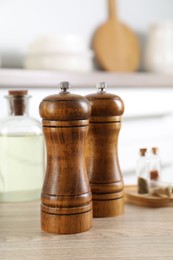 Photo of Salt and pepper mills, spices and bottle of oil on wooden table indoors, closeup
