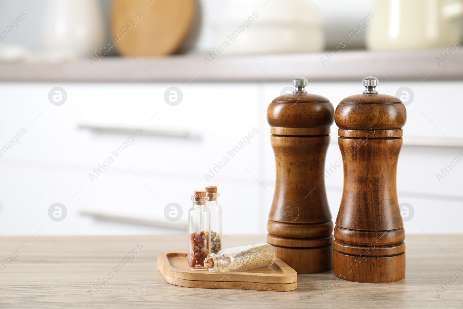 Photo of Salt, pepper mills and spices on wooden table indoors, closeup. Space for text