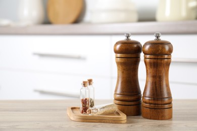 Photo of Salt, pepper mills and spices on wooden table indoors, closeup. Space for text