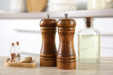 Photo of Salt and pepper mills, spices and bottle of oil on wooden table indoors, closeup