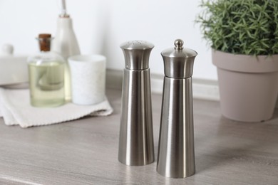 Photo of Metal salt and pepper mills on grey wooden counter indoors, closeup