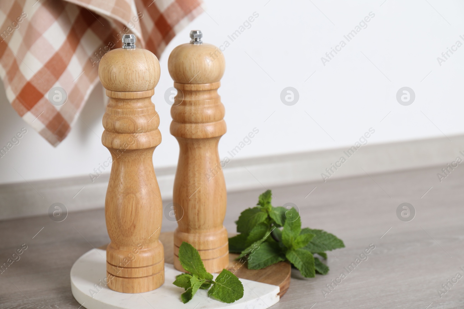 Salt, pepper mills and mint on grey wooden counter near white wall, closeup. Space for text Photo of Salt, pepper mills and mint on grey wooden counter near white wall, closeup. Space for text