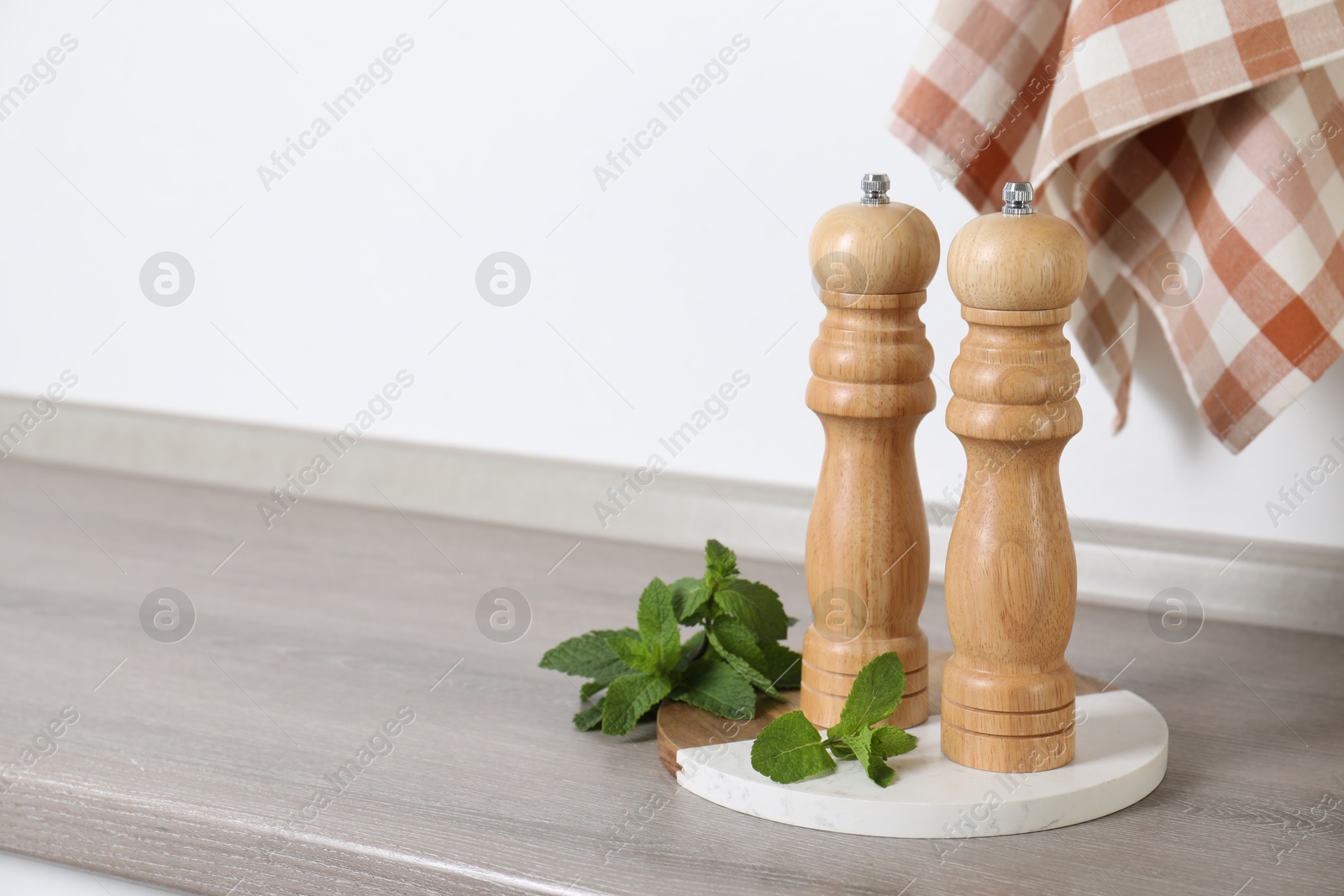 Salt, pepper mills and mint on grey wooden counter near white wall, closeup. Space for text Photo of Salt, pepper mills and mint on grey wooden counter near white wall, closeup. Space for text