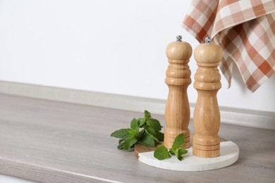 Photo of Salt, pepper mills and mint on grey wooden counter near white wall, closeup. Space for text
