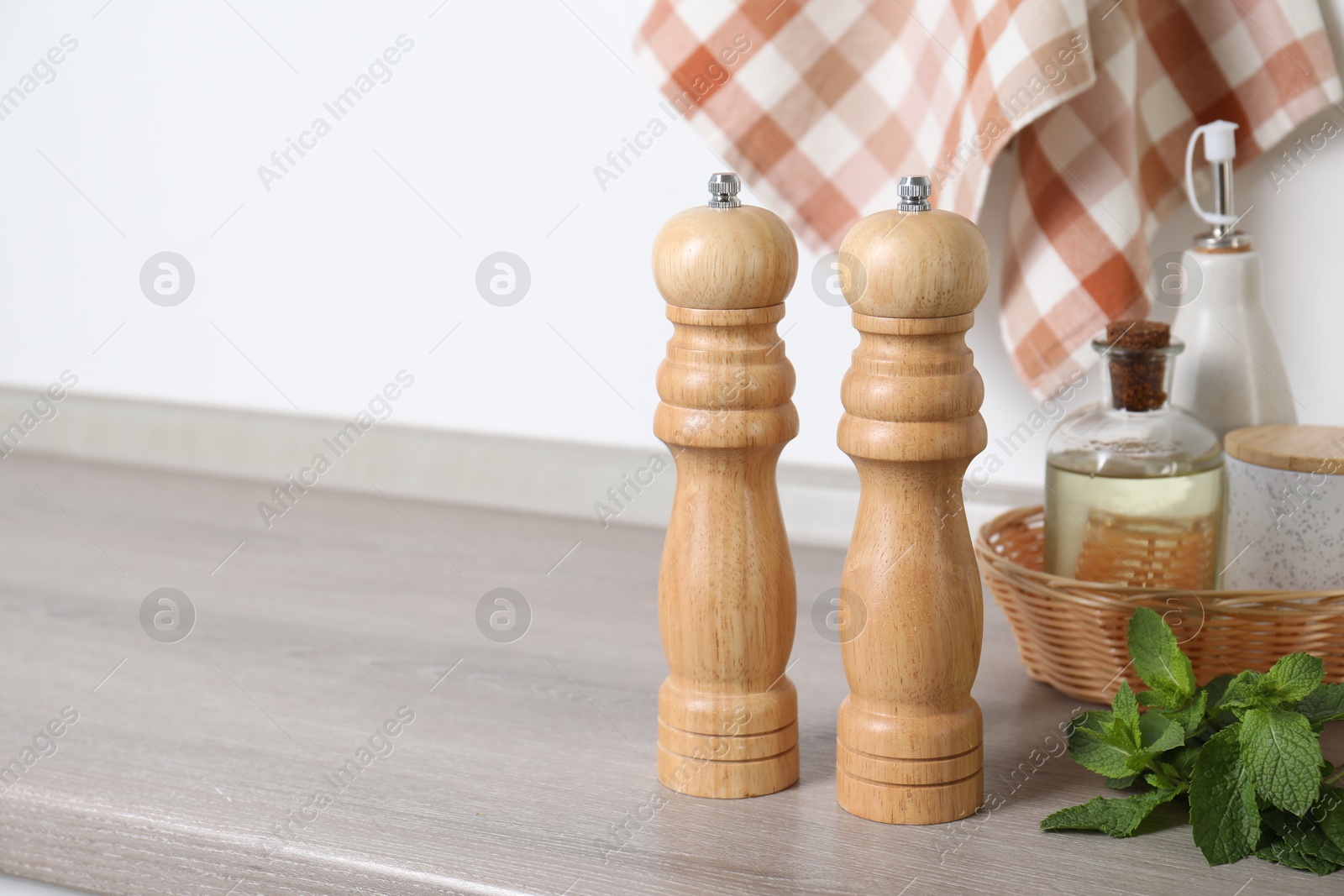 Photo of Salt, pepper mills, bottles of oil and mint on grey wooden counter near white wall, closeup. Space for text
