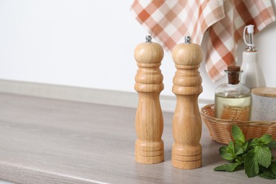 Photo of Salt, pepper mills, bottles of oil and mint on grey wooden counter near white wall, closeup. Space for text
