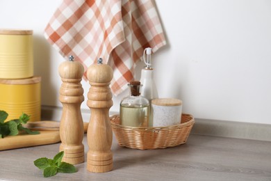 Photo of Salt, pepper mills, bottles of oil and mint on grey wooden counter near white wall. Space for text